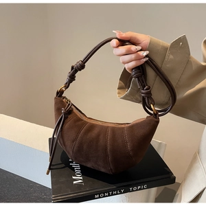 Detail of brown suede croissant bag featuring vertical stitching and knot strap design