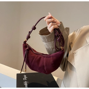 Detail of burgundy suede croissant bag with vertical pleated stitching and knot strap