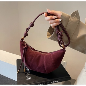 Detail of burgundy crescent bag in matte suede with segmented pleats and knotted strap
