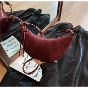 Close-up of burgundy suede croissant bag featuring iconic knot detail and gold hardware