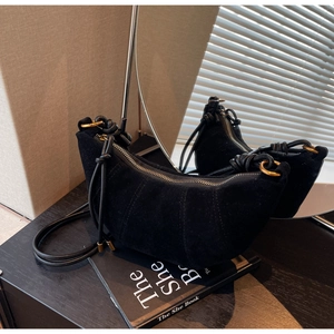 Detail of black suede croissant bag showing knotted strap and smooth zipper closure
