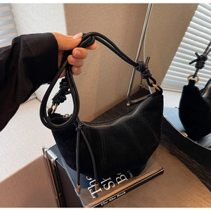 Detail of black suede crescent bag with knot strap and gold metal zipper hardware