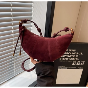 Close-up of burgundy suede croissant bag featuring stitched paneling and knotted strap