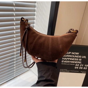 Detail of a brown suede croissant bag featuring curved quilting and metallic zipper