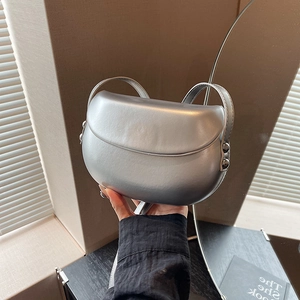Détail d'un sac selle argenté avec finition métallique et clous tenu à la main