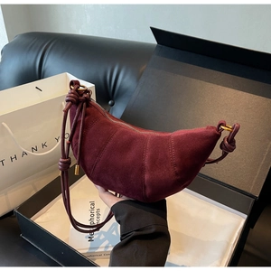 Detail of burgundy suede croissant bag with braided strap knot and gold metal rings
