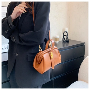 Close-up of bright orange lychee grain leather handbag with golden metal clasp hardware