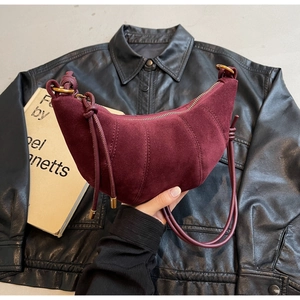 Detail of burgundy frosted suede crescent bag with curved stitching and gold hardware