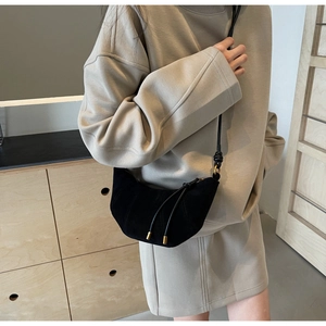 Detail of black suede croissant bag with leather strap on a model in minimalist studio