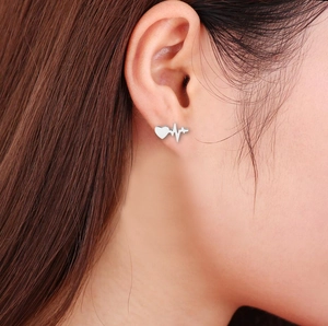 Nahaufnahme von Herzschlag-Ohrstecker aus Silber am Ohrläppchen des Models