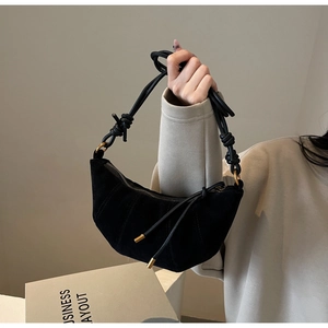 Detail of black suede croissant bag with hand-knotted strap and gold metal hardware