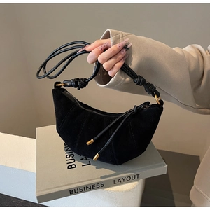 Detail of black suede croissant bag with leather knotted strap and gold hardware