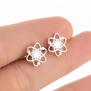 Puces d'oreilles minimalistes en acier inoxydable en forme d'atome entre les doigts