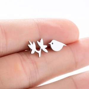 Asymmetric silver bird and leaf stud earrings shown on finger for scale
