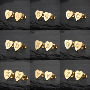 Golden heart-shaped stainless steel earrings with various engraved letters on stone background
