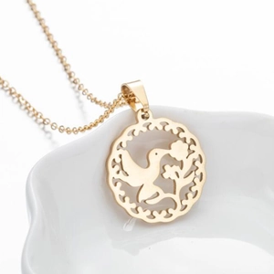 Geometrische goldene Kette mit hohlem Vogel-Anhänger auf weißem Keramik-Tablett