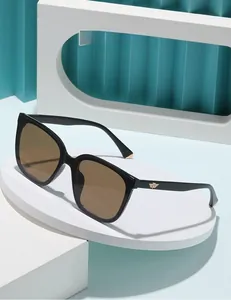 Detail of square sunglasses featuring golden metallic wing logo on a dark brown frame
