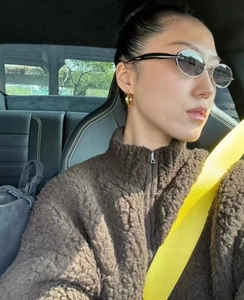 Detailed view of silver oval sunglasses and faux shearling jacket on model in a car