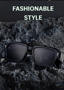 Close-up of square black sunglasses with metal arrow accents on a textured rock background