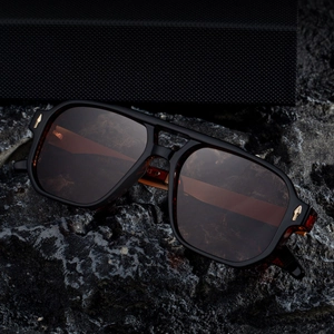 Lunettes de soleil rétro carrées noires brillantes avec détails métalliques dorés sur roche