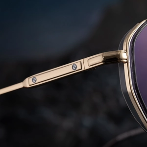 Close-up of gold metal frame sunglasses with purple lenses and circular CD logo hinge