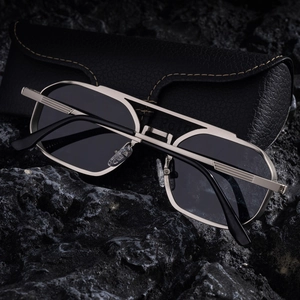 Détail de lunettes de soleil carrées en métal avec double pont sur pierre noire et étui
