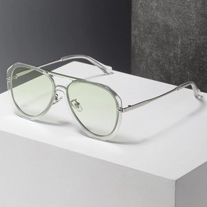 Classic pilot sunglasses with transparent frames and green lenses on a white stone pedestal