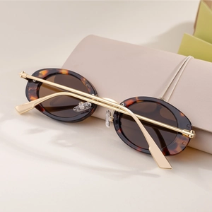 Detail view of oval tortoise shell sunglasses with gold metal temples on leather surface