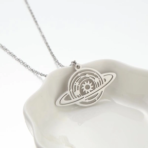 Minimalist stainless steel planet necklace with Saturn pendant in a white ceramic dish