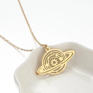 Macro shot of gold planet saturn pendant necklace on white ceramic tray background