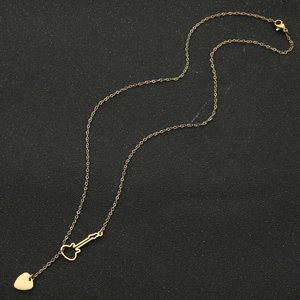 Vue détaillée du collier violon doré avec breloque cœur sur fond noir texturé