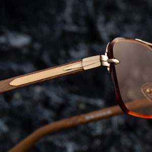 Macro view of golden metal hinges and dark wood grain temples on rimless sunglasses