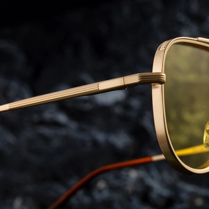 Détail de la charnière en métal doré et du verre ambré sur les lunettes de soleil carrées