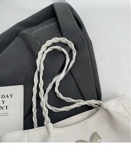 Detail of white tote bag featuring double braided shoulder straps and butterfly metal clasp