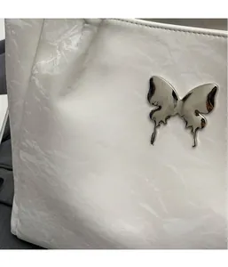 Close-up of white wrinkled leather bag with shiny silver metal butterfly ornament