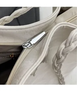Detail of silver zipper and woven handle on a minimalist white faux leather tote bag