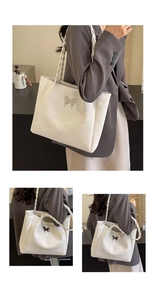 Detail of white tote bag featuring a silver metal butterfly and braided shoulder strap