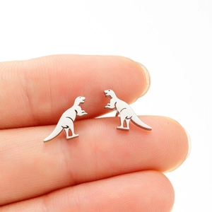 Macro view of dinosaur stud earrings held on finger to show compact miniature size
