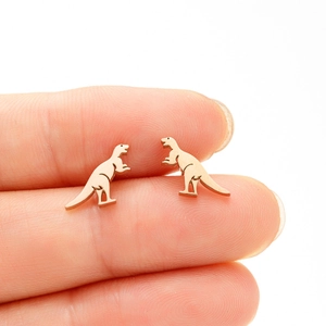 Close-up of a tiny golden dinosaur stud earring held on a fingertip for size scale