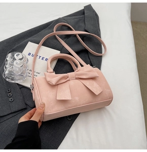 Detailed view of pink suede bow handbag featuring a stylish matte texture and shoulder strap