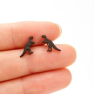 Close-up of small black dinosaur silhouette stud earrings displayed on a fingertip