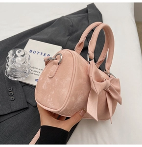 Detailed view of pink suede boston bag featuring a large decorative bow and metal D-rings