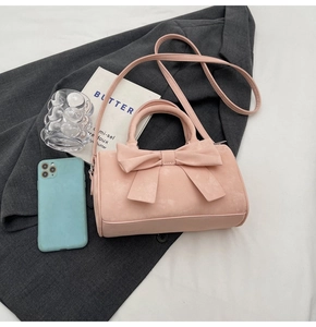 Detailed top view of pink bow cylindrical bag on grey blazer with styling accessories
