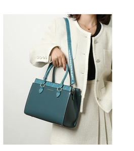 Detail of teal tote bag with crocodile texture and fashion logo on tweed suit