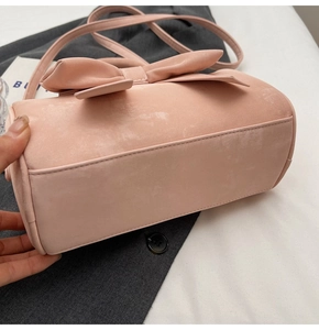 Detailed side view of pink cylindrical crossbody bag with bow and suede finish