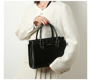 Detail of black tote bag showing crocodile texture contrast and gold metal logo hardware