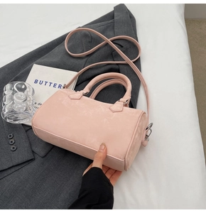 Pink cylinder handbag with suede texture featuring double handles and a detachable strap