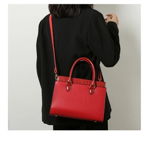 Red leather tote bag with crocodile texture details worn by a model in a black blazer