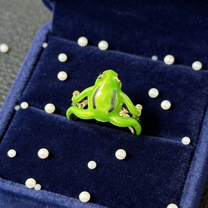 Cute green enamel frog hugging ring with adjustable gold metal band on blue velvet