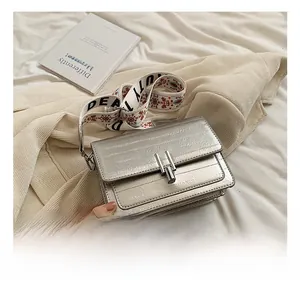 Detail of silver textured square bag featuring a wide ethnic floral pattern strap